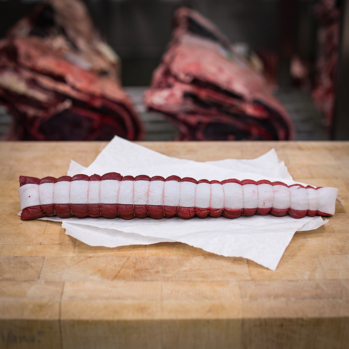 Filet de chevreuil sauvage cru d’environ 500 g, paré, bardé de lard de porc et ficelé, sur un billot en bois