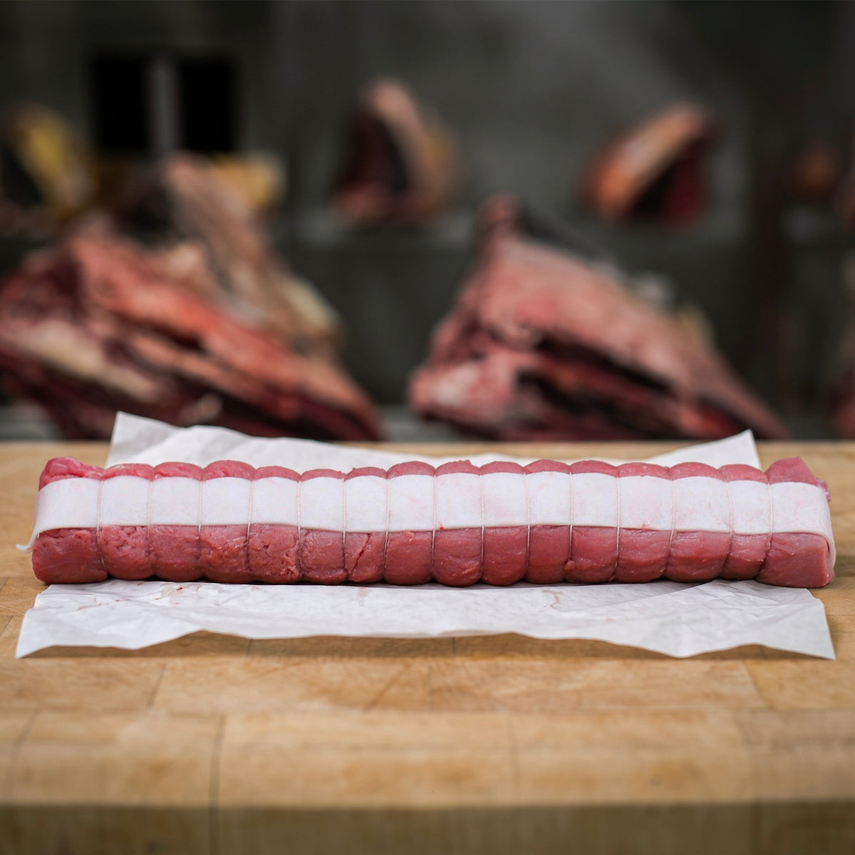 Filet de marcassin cru d’environ 500 g, entouré de bandes de lard de porc et ficelé, sur un billot en bois