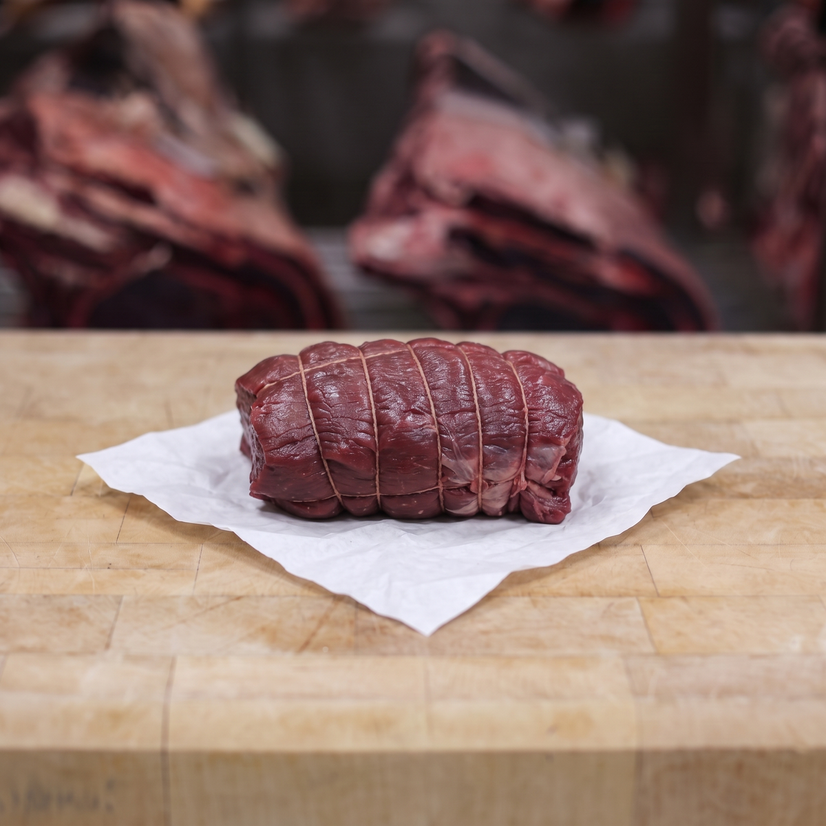 Rôti de chevreuil sauvage cru d’environ 700 g, tenu dans un filet de boucher, posé sur un billot en bois